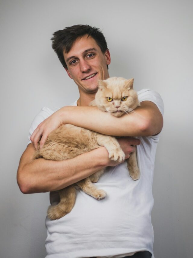 man in white crew neck t-shirt carrying brown cat